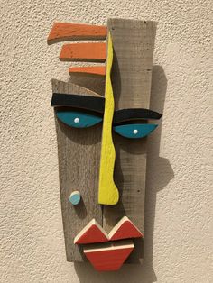 a wooden mask hanging on the side of a building with blue eyes and yellow hair