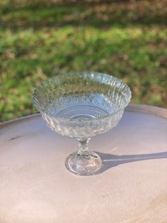 an empty glass bowl sitting on top of a wooden table in front of some grass