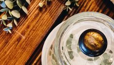 an empty glass jar sitting on top of a wooden table next to some leaves and flowers