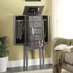 a gray jewelry cabinet sitting in front of a window next to a chair and rug