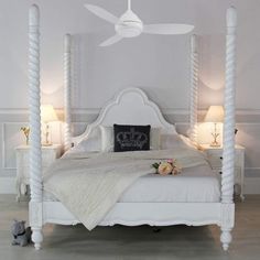 a white bed sitting next to two lamps on either side of the bed and a ceiling fan