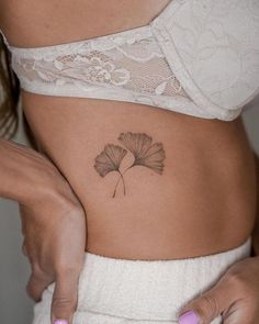 a woman's stomach with a small leaf tattoo on her left side ribcage