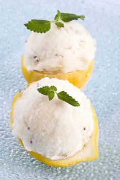 two lemon halves with ice cream and mint sprig on top, sitting on a blue surface