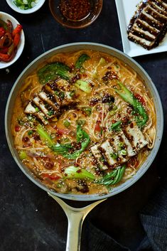 a pan filled with noodles and chicken on top of a table next to other dishes