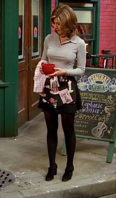 a woman is standing on the sidewalk in front of a store holding an apple and looking at her cell phone