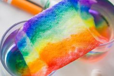 a close up of a rainbow colored substance in a cup with two markers on the side