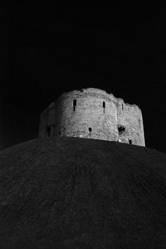 a black and white photo of an old castle at night with the moon in the sky