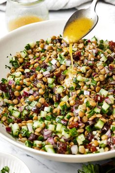 a white bowl filled with salad and dressing being drizzled over the top