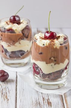 two desserts with cherries and whipped cream in glasses on a white wooden table