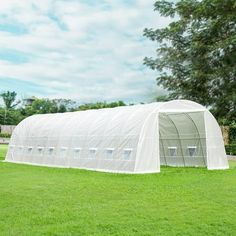 a large white greenhouse in the middle of a grassy field with trees and bushes behind it