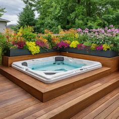 a hot tub sitting on top of a wooden deck next to flowers and trees in the background