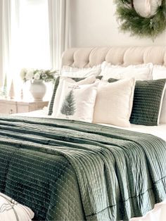 a bed with green and white comforter in a bedroom next to a window filled with wreaths