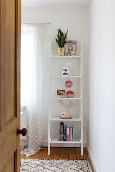 a white shelf with books and plants on it in a room next to a door