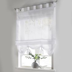 a bathroom window with white curtains and a vase filled with flowers next to the toilet