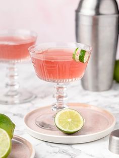 two glasses filled with pink lemonade and garnished with limes on the side