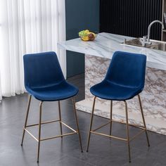 two blue chairs sitting next to each other in front of a marble counter top with a bowl of fruit on it