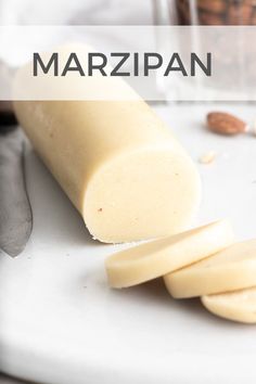 a white cutting board topped with sliced bananas and almonds next to a jar of marzipan