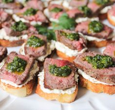 small appetizers with meat and pesto on them are arranged on a white plate