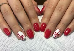 two hands with red and white nail polishes on their nails, one has a bow