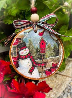 a snowman ornament hanging from a plant with red flowers in the background