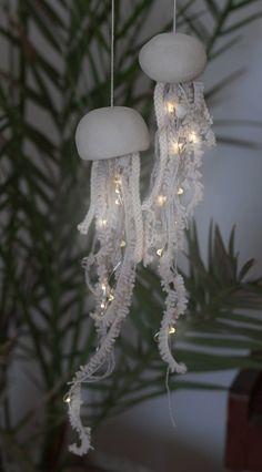 two white jellyfish lights hanging from strings in front of a potted palm tree