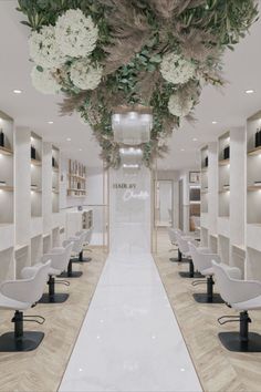 the interior of a hair salon with white chairs and flowers hanging from the ceiling above