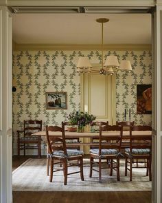 a dining room table and chairs in front of a wall papered with floral designs