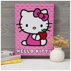 a hello kitty painting sitting on top of a table next to some books and a vase