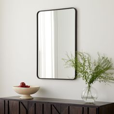 a mirror on the wall next to a vase with a plant and fruit in it