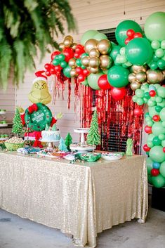 a table topped with lots of green and red balloons next to a wall covered in christmas decorations