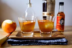 two glasses filled with liquid sitting on top of a wooden tray next to an orange