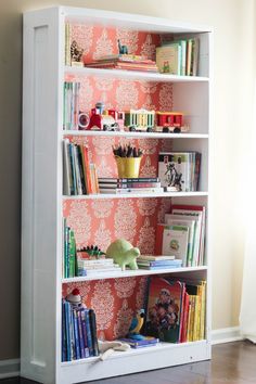 a bookshelf filled with lots of books next to a wallpapered wall