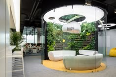 an office with plants on the wall and round couches in front of glass walls