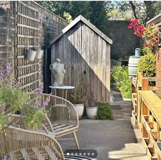 an outdoor patio with chairs and tables next to a wooden fenced in area filled with potted plants