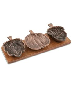 three pieces of metal sitting on top of a wooden tray with leaves and acorns