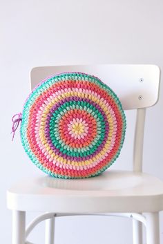 a white chair with a colorful crocheted round pillow on it's back