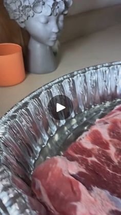 raw meat is being prepared in an aluminum foil pan on a counter top next to a statue