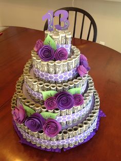 a three tiered cake decorated with purple and green paper flowers on a wooden table