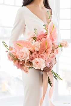 a woman in a white dress holding a bouquet of pink flowers and greenery on her wedding day