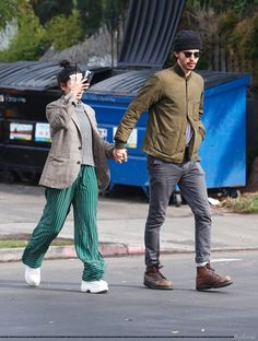 a man and woman walking down the street with their cell phones in hand while holding hands