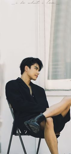 a young man sitting in a chair with his legs crossed and wearing black shoes, looking off to the side