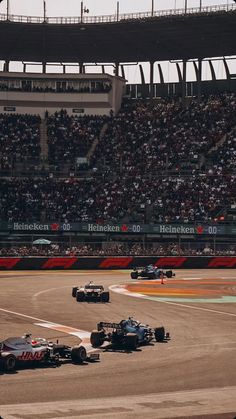 a group of racing cars driving down a race track in front of an empty crowd