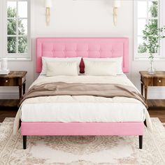 a bed with pink headboard and pillows in a white room next to two windows