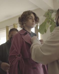 a woman in a pink trench coat getting her tie put on