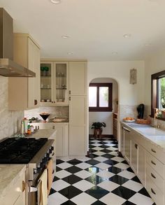 a black and white checkered floor in a kitchen with an oven, sink, stove top and cabinets