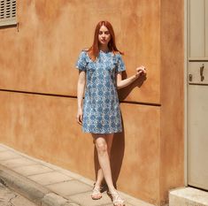 a woman standing on the side of a building next to a wall with her hands in her pockets