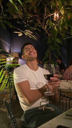 a man sitting at a table with a glass of wine in his hand and smiling