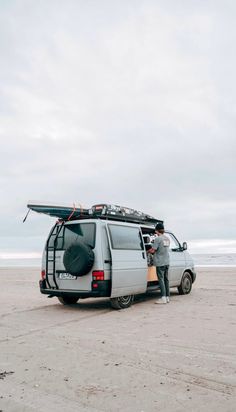 a man standing next to his van with surfboards on the roof