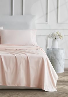 a bed with pink sheets and pillows on top of it next to a white vase