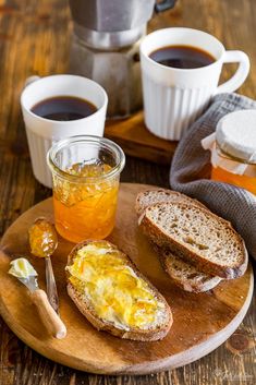 there is a plate with bread, butter and jam on it next to two cups of coffee